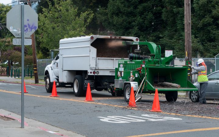 Chipper truck and wood chipper parked behind traffic cones on a city street