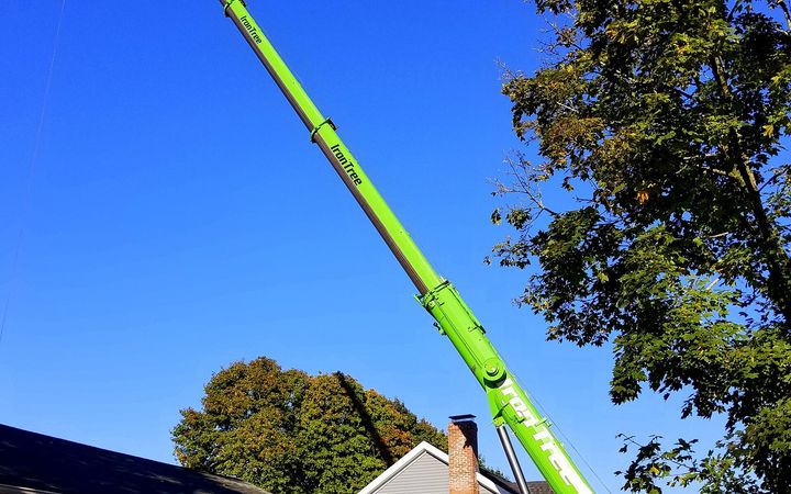 Green mobile crane with its boom raised beside a house and a large tree