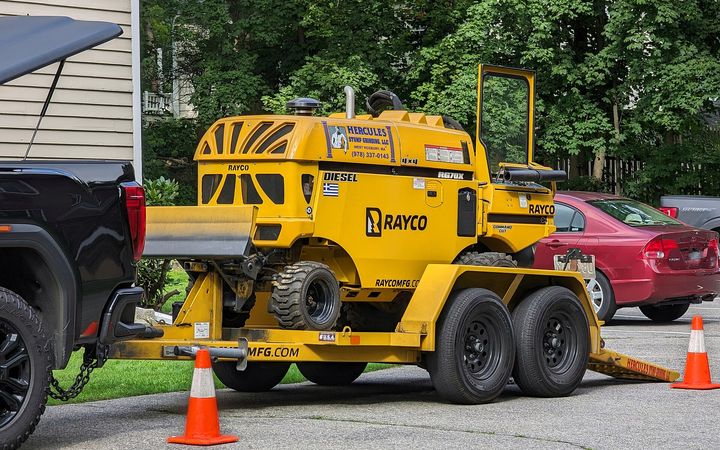 Yellow stump grinder on a trailer parked at the curb of a residential street